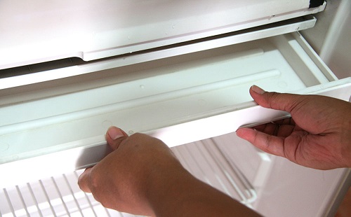 мастер по ремонту холодильника вынимает поддон чтобы помыть его от запаха