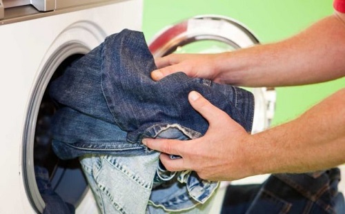 Мужчина достает их стиральной машинки постиранные чистые джинсы