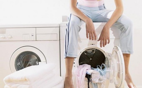 уставшая девушка сидит свесив ноги на стиральной машинке